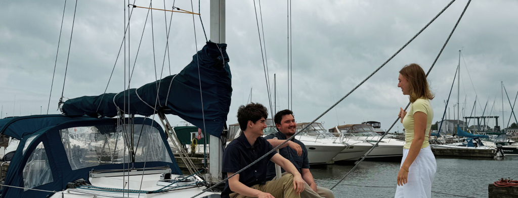 Three young people sitting on a sail boat in the marina