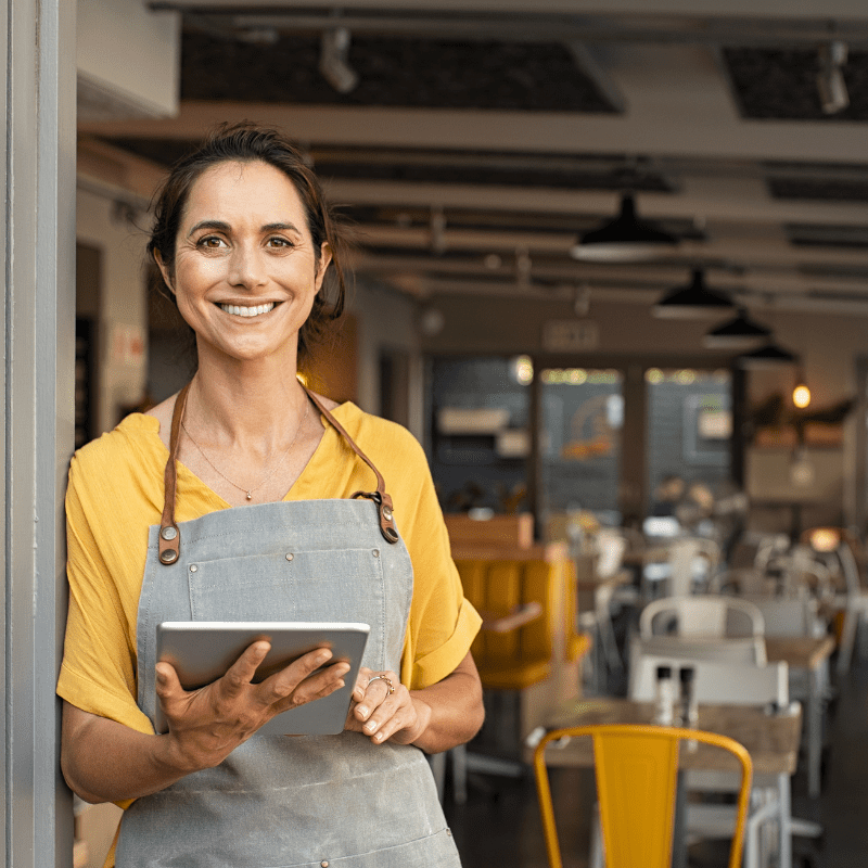 Female small business owner outside her restaurant holding a tablet.