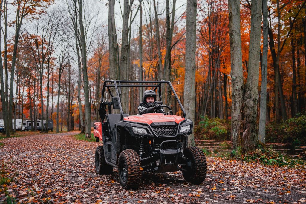 ATV with driver wearing helmet. Riding through trail scattered with fall leaves.