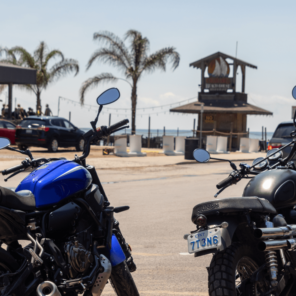 Motorcycles parked at beach, in front of Callahan's Beach House tiki bar with palm trees in the background.