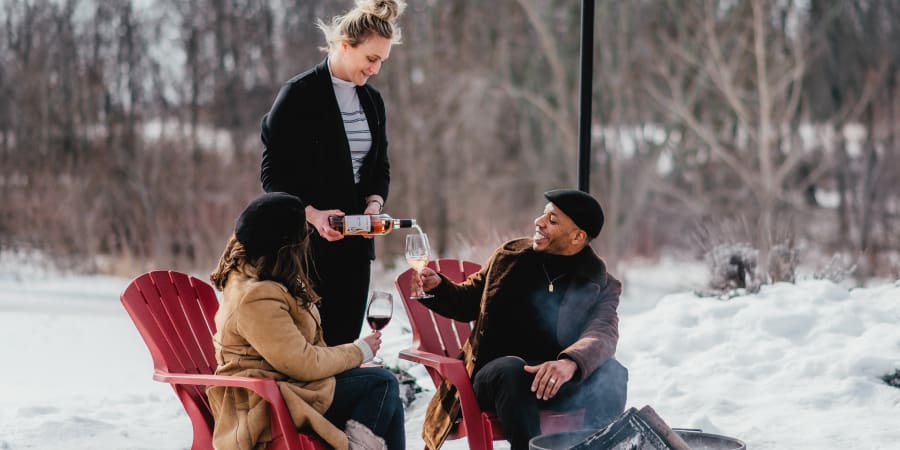 A woman pours wine into glasses of two visitors to the winery. Winter setting.